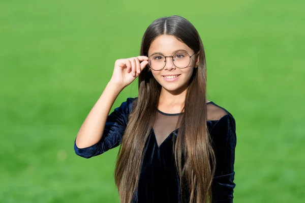Boldog kis lány hosszú haj divat fekete ruha fix korrekciós szemüveg szépség megjelenés zöld fű napos nyári szabadban, optikusok — Stock Fotó