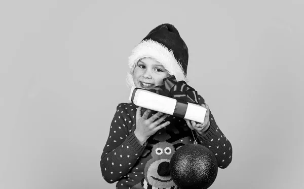 Förberedelser inför det nya året. Dags för julshopping. Leksaksaffär och presenter till barn. Ett leende barn i tomteluva. Låt julen vara ljus. barndoms lycka. liten nisse hålla gåva och dekoration boll — Stockfoto
