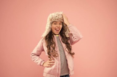 Kış moda konsepti. Soğuk hava için sıcak şapka. Sahte kürk trendi. Uzun kıvırcık saçlı kız, pembe kulaklıklı kürk şapka takıyor. Yumuşak tüylü aksesuar. Çocuk uzun saçlı yumuşak kürk şapkalı Yumuşaklığın tadını çıkar