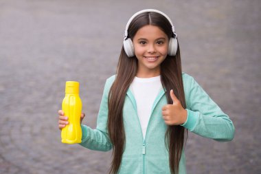 Çocuk vücudunda su dengesi. Öğle yemeği zamanı. Sıvı kaybı. Sağlıklı bir yaşam tarzı. çocukluk mutluluğu. Mutlu çocuk dışarıda kulaklık takıyor. Okula dönüyorum. Genç kız spor şişesini tutuyor. başparmak hareketi