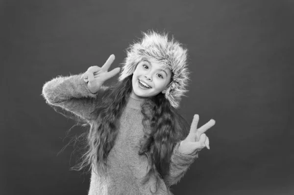 Ειρήνη σε όλους. Χειμερινή περίοδος. Μικρή έννοια fashionista. Παιδικό μακρυμάνικο καπέλο. Χειμερινή μόδα. Ζεστό καπέλο για κρύο χειμώνα. Ένα κορίτσι χαμογελάει κόκκινο φόντο. Μαλακό τριχωτό εξάρτημα — Φωτογραφία Αρχείου