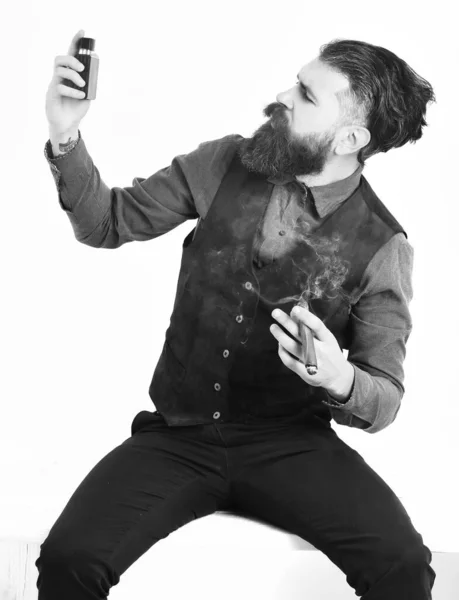 Homem barbudo fumar charuto com rosto sério, segurando perfume — Fotografia de Stock