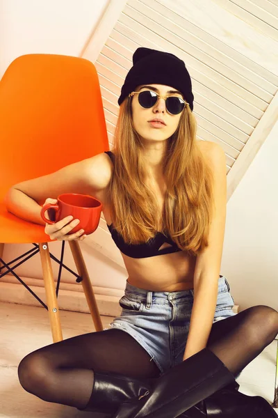 Ganska sexig kvinna i solglasögon på orange stol med kopp — Stockfoto