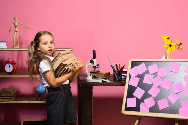 Menina carrega pilha de livros para mesa com microscópio — Fotografia de Stock