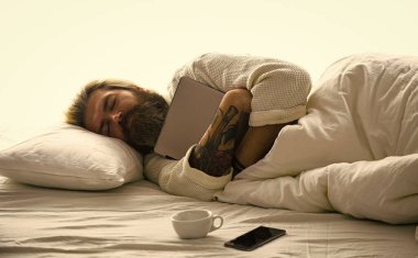 Aletlerden ayrılmaz. İyi uykular. Sosyal ağlara bağımlılık. Mavi Işık Efekti. Uykulu yüzlü bir adam dizüstü bilgisayarla yastığa uzanır. Derin uyku konsepti. Sakallı ve bıyıklı adam uyuyor.