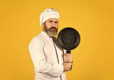 Nonstick cookware. Frying without oil. Professional kitchenware. Bearded chef preparing breakfast. Nonstick pan for frying. Enameled cooking vessels. Man hold pan. Frying meal. Healthy food clipart
