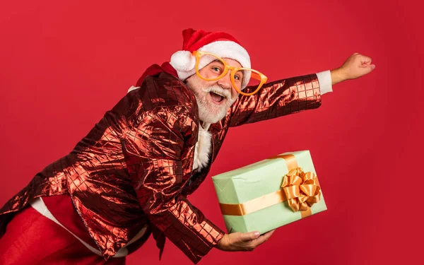 Echte gevoelens. Grappige senior man in kerstman kostuum. Gelukkig nieuwjaar 2021. Vrolijk kerstfeest. bebaarde santa in hoed vliegen op rode achtergrond. Kerstcadeautjes en cadeautjes. wintervakantie vreugde — Stockfoto