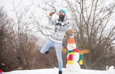 Sakallı hippi yakışıklı örgü şapka dışarıda karla oynuyor. Soğuk kış gününüzde iyi eğlenceler. Kar yağsın. Noel tatili. Aktif yaşam tarzı. Kar oyunları. Temiz hava iyi gelir. Kardan adam konsepti