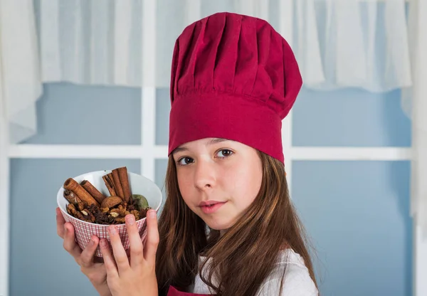 요리 모자를 쓴 작은 소녀가 양념과 조리법이 담긴 접시를 들고 있다 — 스톡 사진