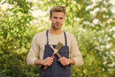 Barbekü partisi. Piknik konsepti. Barbekü şefi. Yemek pişiren yakışıklı adam. Hamburger pişiriyorum. Adam barbekü malzemelerini tutuyor. Izgara yemek. Barbekü aletleri. Yaz haftasonu. Açık havada et kızartmak için araçlar