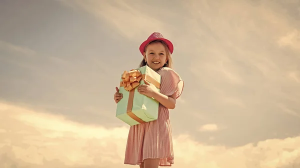 Mała dziewczynka trzyma pudełko prezentów. Mały dzieciak z pudełkiem prezentów. Wszystkiego najlepszego. szczęście z dzieciństwa. Świętujmy wakacje. dziecko w letni dzień na tle nieba. czas na zakupy — Zdjęcie stockowe