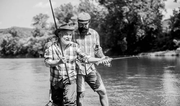 Pörgőtekerccsel horgászni. Napfényes nyári nap a folyónál. Halászcsalád. Hobbi sport. Békésen horgászunk. Apa és fia horgásznak. Rod szerelés. Halászfelszerelés. Nagyapa és érett férfi barátok — Stock Fotó