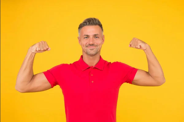 Güçlü atletik adam kırmızı tişörtle gülümsüyor kaslı kollar sarı arka plan, güç — Stok fotoğraf