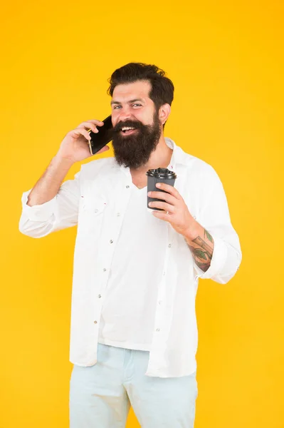 Cara alegre com bigode e barba beber café e falar no smartphone. homem barbudo maduro falar ao telefone enquanto bebe café da manhã. bebida quente em copo de papel. vida moderna — Fotografia de Stock