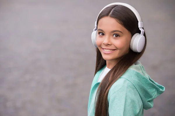 Miúdo ouve música ao ar livre. andando com melodia favorita. educação conceito online. felicidade infantil. aprendizagem electrónica de menina estudante. espaço de cópia. criança sorridente feliz gosta de ouvir música em fones de ouvido — Fotografia de Stock