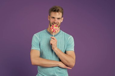 Bekarlar Günü. Tatlı yerken mutlu ol. Mutluluğun sembolü. Adam lolipop yiyor. Gülümseyen adam lolipop tutuyor. Tatil konsepti. Bekarlar için gayri resmi tatil. Guy Lolipop menekşe şekeri arka planı. Tatlı çocuk.