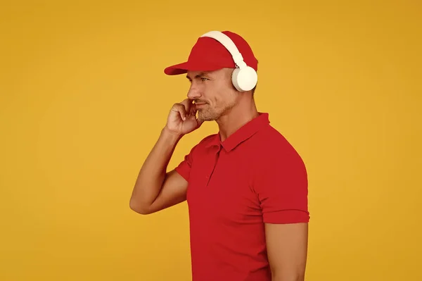 Audio guide. Man in headphones on yellow background. Incoming call. Worker in uniform with earphones. Assistant call center help find solution. Guy call service worker. Man listen music headphones