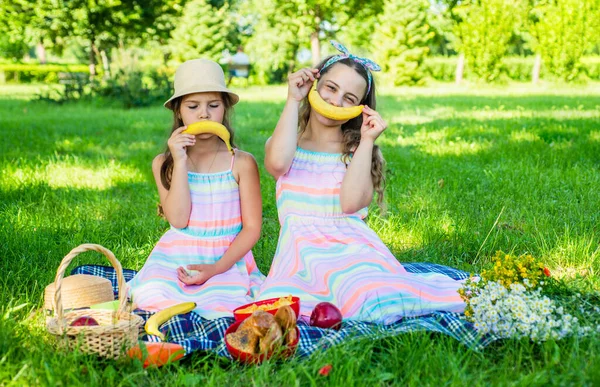 Los niños pequeños y divertidos hacen emoticonos sonrientes tristes y felices con fruta de plátano en el picnic sobre hierba verde en el paisaje soleado del verano, diversión —  Fotos de Stock
