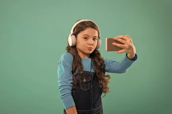Νιώθω παιχνιδιάρης και αστείος. μικρό παιδί βιντεοκλήση στο smartphone. μικρό κορίτσι κρατήσει το κινητό τηλέφωνο. blogging στη σύγχρονη ζωή. Μαθήτρια χρησιμοποιεί νέα τεχνολογία. ζουν σε εικονικό κόσμο. παιδί selfie στα ακουστικά — Φωτογραφία Αρχείου