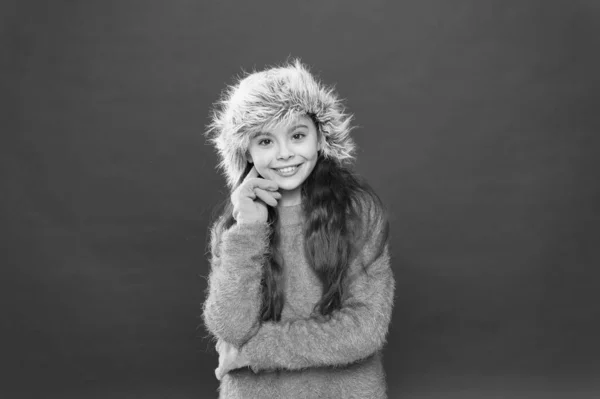 Ένα κορίτσι χαμογελάει κόκκινο φόντο. Μαλακό γούνινο αξεσουάρ. Χειμερινή περίοδος. Μικρή έννοια fashionista. Νιώθω τόσο άνετα. Παιδικό μακρυμάνικο καπέλο. Χειμερινή μόδα. Ζεστό καπέλο για κρύο χειμώνα — Φωτογραφία Αρχείου