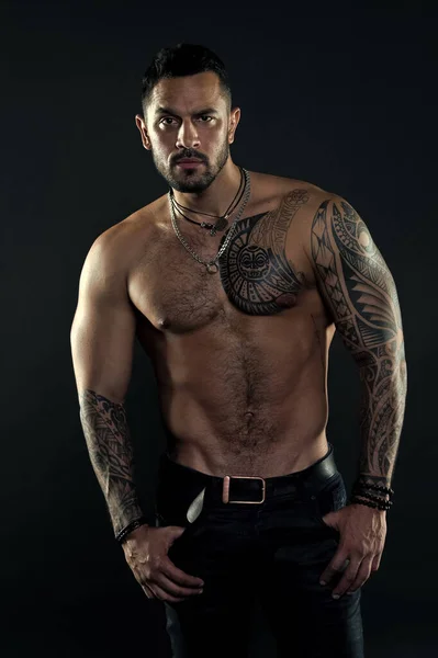 Jewelry for real men. Bearded man with tattooed torso. Macho sexy bare torso. Fit model with tattoo art skin. Sportsman or athlete with beard and hair. Sport and fitness. Masculinity. Muscular torso