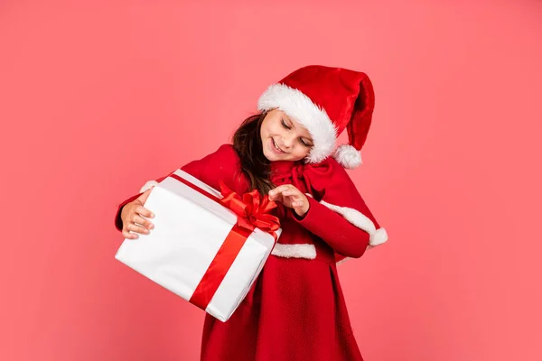 God jul och god jul. Vinterlov. Julklappsshopping. Ett presentpaket. Kärleksfulla drömmar. Boxningsdag. Liten bedårande flicka Santa hatt hålla presentförpackning. Grabben hålla nuvarande rutan röd bakgrund — Stockfoto