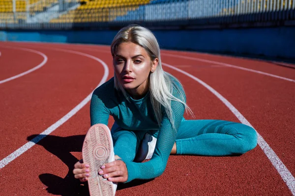 athletic female coach in fitness costume stretch on running track, flexibility