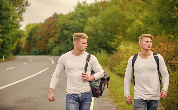 Summer vacation. Tourist traveler travel auto stop. Budget travelers. men backpacks walking together by road. twins walking along road. Adventure and discovery. Man with backpack hitchhiking on road — Stock Photo, Image