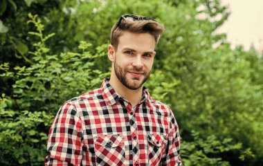 Modayı takip ediyorsun. Sakallı yakışıklı adam. Tıraşsız genç adam. Parkta kareli kıyafetler giyen seksi adam poz veriyor. Kendine güveni tam, kentli tişörtle gülümseyen genç bir adam. kot moda tarzı