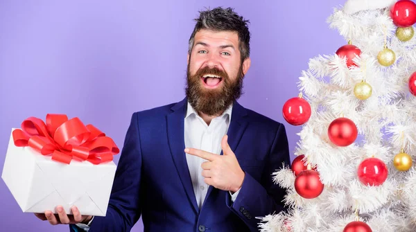 Best gifts for colleagues. Office christmas party. Man bearded hipster formal suit near christmas tree. Christmas gifts and decorations. Secret Santa concept. Winter holidays. Christmas greetings