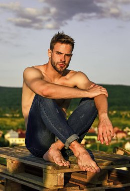 Yaz gezileri kitabı. Kaslı, çıplak gövde. Altı paket kaslı göğüs. Açık havada mavi gökyüzü arka planı. Erkek güzellik konsepti. Atletik yakışıklı maço kot pantolon giyiyor. Kaslı vücut. Fitness modeli
