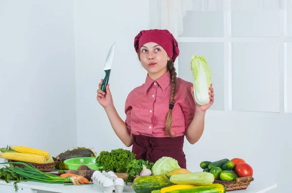 Wat te koken. vol vitaminen. Het kind draagt kokskleding en hoed. Tienermeisje bereidt Chinese kool voor. verse rauwe groenten. Tijd om te eten. Gelukkig kind koken in de keuken. alleen gezond en biologisch voedsel — Stockfoto