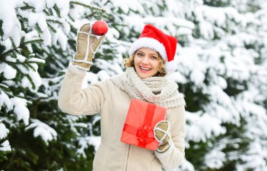 Ne güzel bir sürpriz. Beyaz karla kaplı kış ormanı. Açık hava mükemmel bir ruh halidir. Mutlu kadın hediye kutusunu tutar. Noel ağacı süslemeli kız. Bayan Kırmızı Noel Baba şapkası kürk ağacında