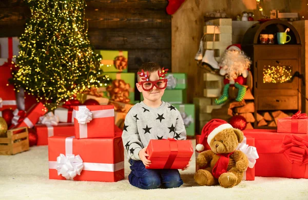 Öffnet sein Weihnachtsgeschenk. Frohe Weihnachten. Glückliche Kinderparty-Brille. Sohn bereit, Winterurlaub zu feiern. kleiner Junge mit Weihnachtsgeschenk. Kinder halten dekorativen Ball. Bärenspielzeug für Weihnachten — Stockfoto