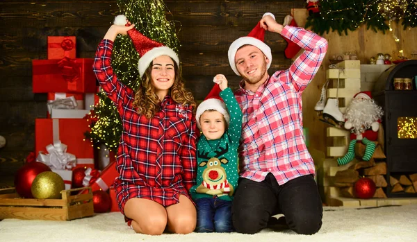 Kerstmis is tijd om te geven. Vrolijk kerstfeest. Mam, pap en het kleine kind hebben plezier. Gelukkig gezin viert nieuwjaar. Ouders met zoon dragen kerstmuts. vader en moeder met kind blijven thuis op vakantie — Stockfoto