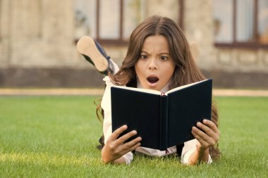 Ders dışı okumalar. Dışarıda kitap okuyan şirin küçük bir çocuk. Temel eğitim. Sevimli küçük kız okumayı öğreniyor. Konsept çalışıyorum. Okul üniforması en sevdiği kitapla çimlerin üzerinde yatıyor.