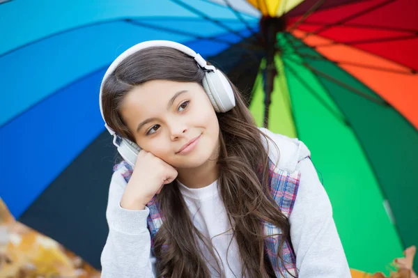 幸せな子供はカラフルな傘の下でヘッドフォンを着用します。女の子は音楽を聞く。子供は秋の森でリラックス。公園に落ち葉。学校に戻って。オンライン教育です。梅雨の時期 — ストック写真