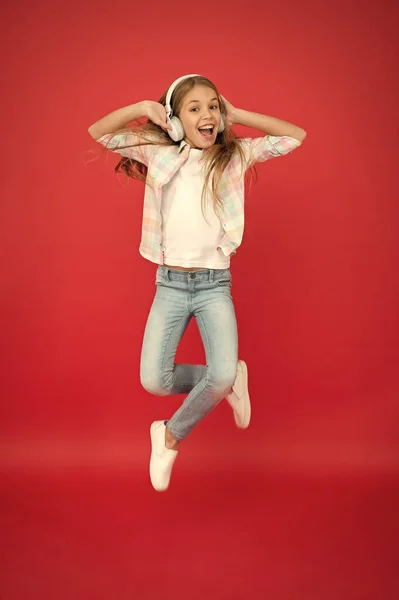 Creo que puedo volar. Chica escuchando música gadget moderno. Niño feliz con auriculares inalámbricos saltando. Auriculares estéreo. Niño usando tecnología moderna. Un niño moderno. Sonido perfecto. Alegría sin fin — Foto de Stock