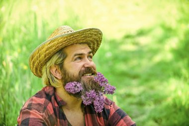 Parlak yaşa. Hasır şapkalı rahat bir çiftçi. Yetişkin bahçıvan yeşil çimlerde rahatlar. Bahar doğasının tadını çıkar. Yaz sezonu leylakla. Vahşi çiftlik hippisinin uzun ve sağlıklı sakalı var. saçtaki çiçek
