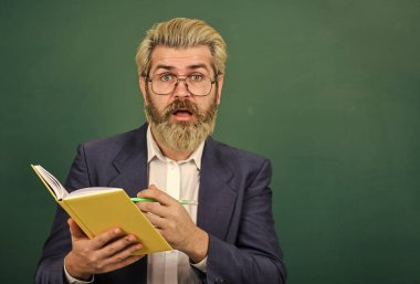 Ders kitabı olan bir öğretmen. Tecrübeli öğretmen. Uygun kurslar seçiliyor. Kitabı olan öğretmen konuyu açıklar. Kara tahtanın önündeki adam. Üniversite ve lise. Edebiyat konusu. Kitap okumak