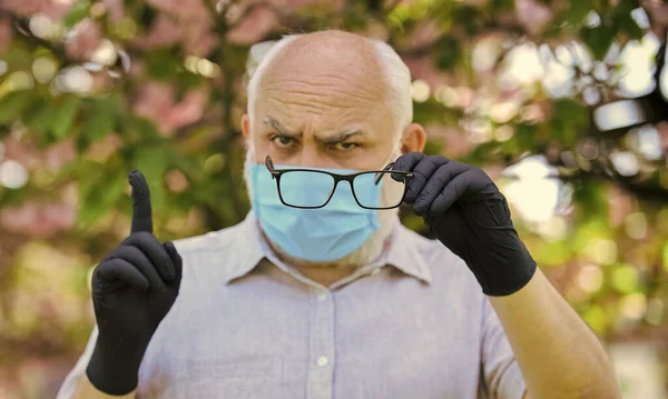 Beschermen en tegen virusinfectie. Beperk de verspreiding van infecties. Senioren geloven desinformatie over covid-19. Senior man draagt gezichtsmasker en handschoenen buiten. Infectie is in de lucht — Stockfoto