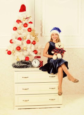 Küçük kız Noel Baba şapkası Noel hediyesini karşılıyor. Gelmiş geçmiş en iyi hediye. Heyecanın yerini güçlü bir tatmin aldı. Mutlu yıllar konsepti. Çocuk, Noel ağacının yanına otur. Oyuncak ayı hediyesini tut.
