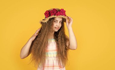 Neşe dolu. çiçek kompozisyonu. Sarı arka planda hasır şapkalı kız. Mutlu çocukluk. Kadın kuaför salonu. Çiçekli güzel kız. Küçük kız pembe çiçekli bir şapka takıyor.