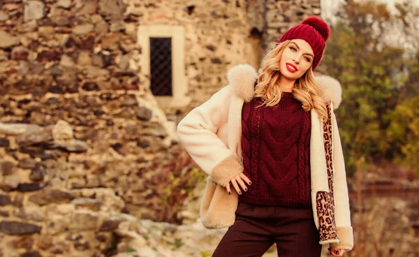 Treffer der Saison. Bleiben Sie warm und modern. Frau trägt pelzigen Mantel. Winterkleidung. Kleiderschrank für kaltes Wetter. Mädchen stehen neben steinernen Ruinen. Schicker Mantel. Schafsfell aus Naturwolle. Pelz auf Kapuze — Stockfoto