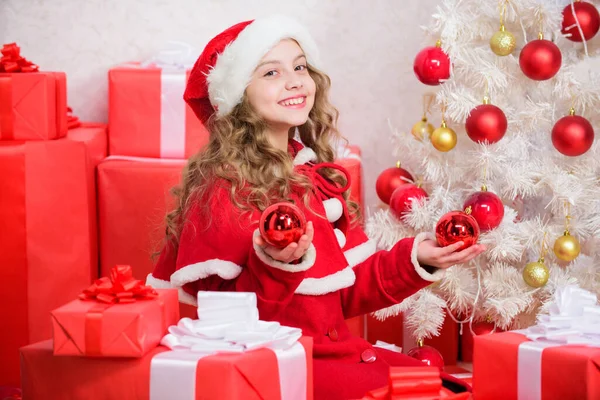 Приєднуйтесь до святкування Різдва. Дівчина щаслива чарівна Санта Клаус біля ялинки. Малюк прикрашає ялинку червоними прикрасами. Захоплені святкові заходи. Дитина насолоджується традицією. концепція напередодні Різдва — стокове фото