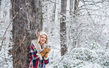 Şapkalı bir kadın ormanda çay içiyor. Yürüyüş ve seyahat. Yürüyüş yapan kız bir fincan sıcak kahve içer. Kış macerası. Seyahat tutkusu. Kış yürüyüşü. Isın biraz. Kadın kış içkisi. Kız sıcak şarabın tadını çıkarıyor.