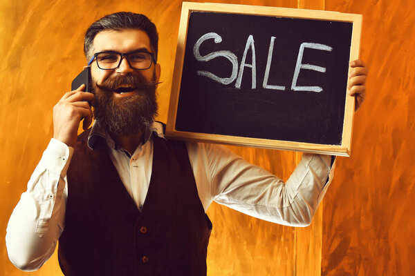 Bearded man, brutal caucasian hipster with smartphone holding sale inscription