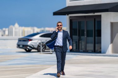 Successful businessman walking with suit in parking. Mature businessman in suit having business call. Corporate business. Rich businessman in suit. Business portrait. Daily schedule.