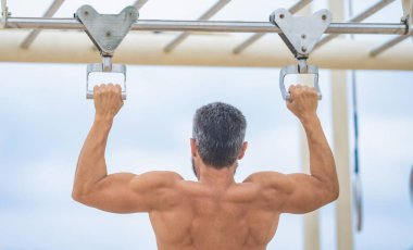 Muscular biceps and triceps. Man pullup. Muscular man sportsman with strong back muscle. Sport pullup workout. Man sportsman pulling exercise. Man muscular back athlete doing pull up in outdoor gym.