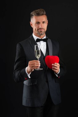 Celebrating success. Cheers for engagement. Mature man has formal look. Celebrate with champagne. Cheering and celebrating. Elegant tuxedo man hold glass of champagne isolated on black.